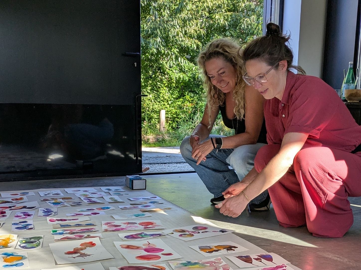Two participants crouched on the atelier floor, looking at rows of ink paintings made during the workshop.