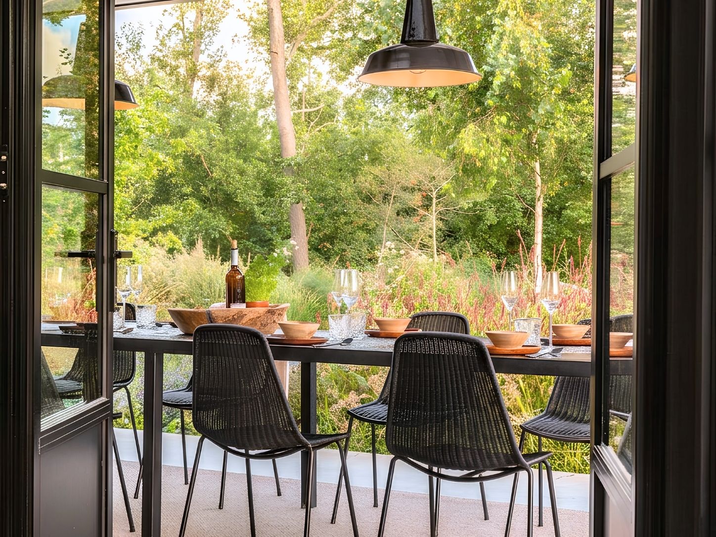 A laid table seen through open steel doors, with the late-summer garden behind it.