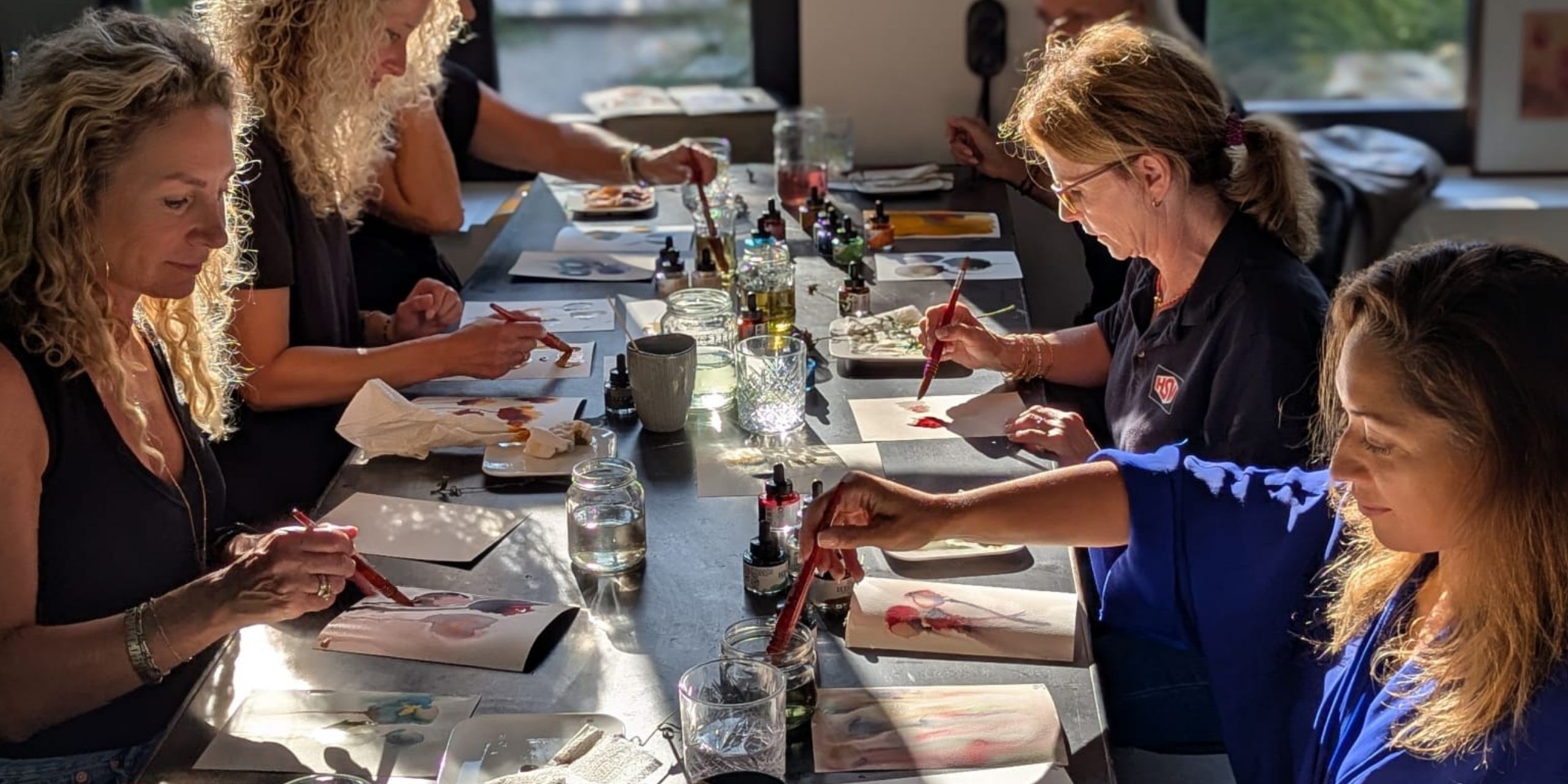 Participants painting with ink at the long table in the atelier, in low afternoon sun.