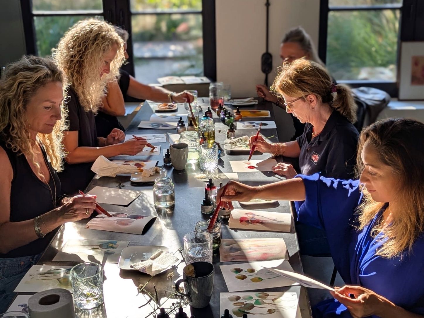 Participants painting with ink at the long table in the atelier, in low afternoon sun.
