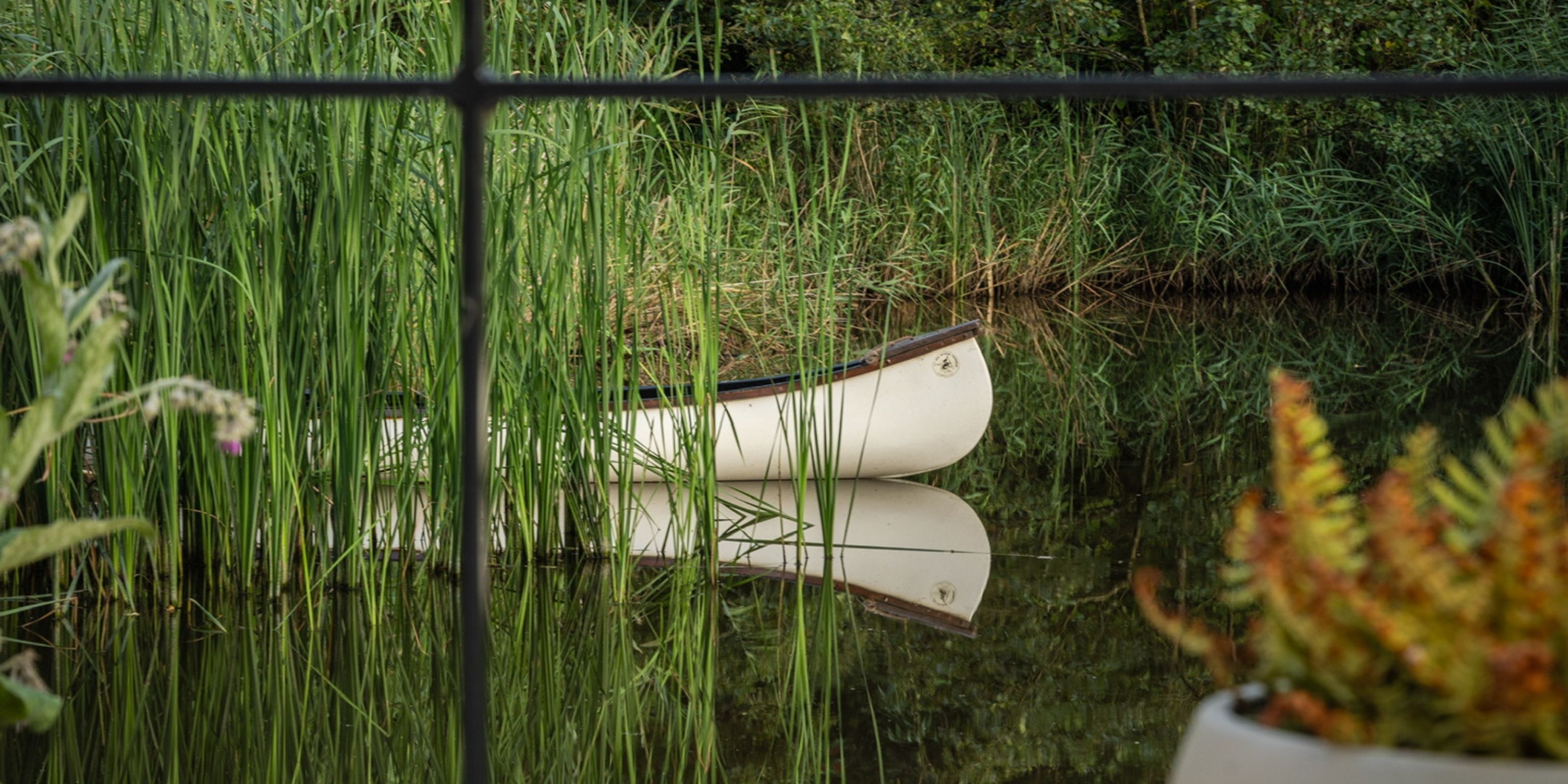 A white canoe among the reeds, mirrored in the dark water.