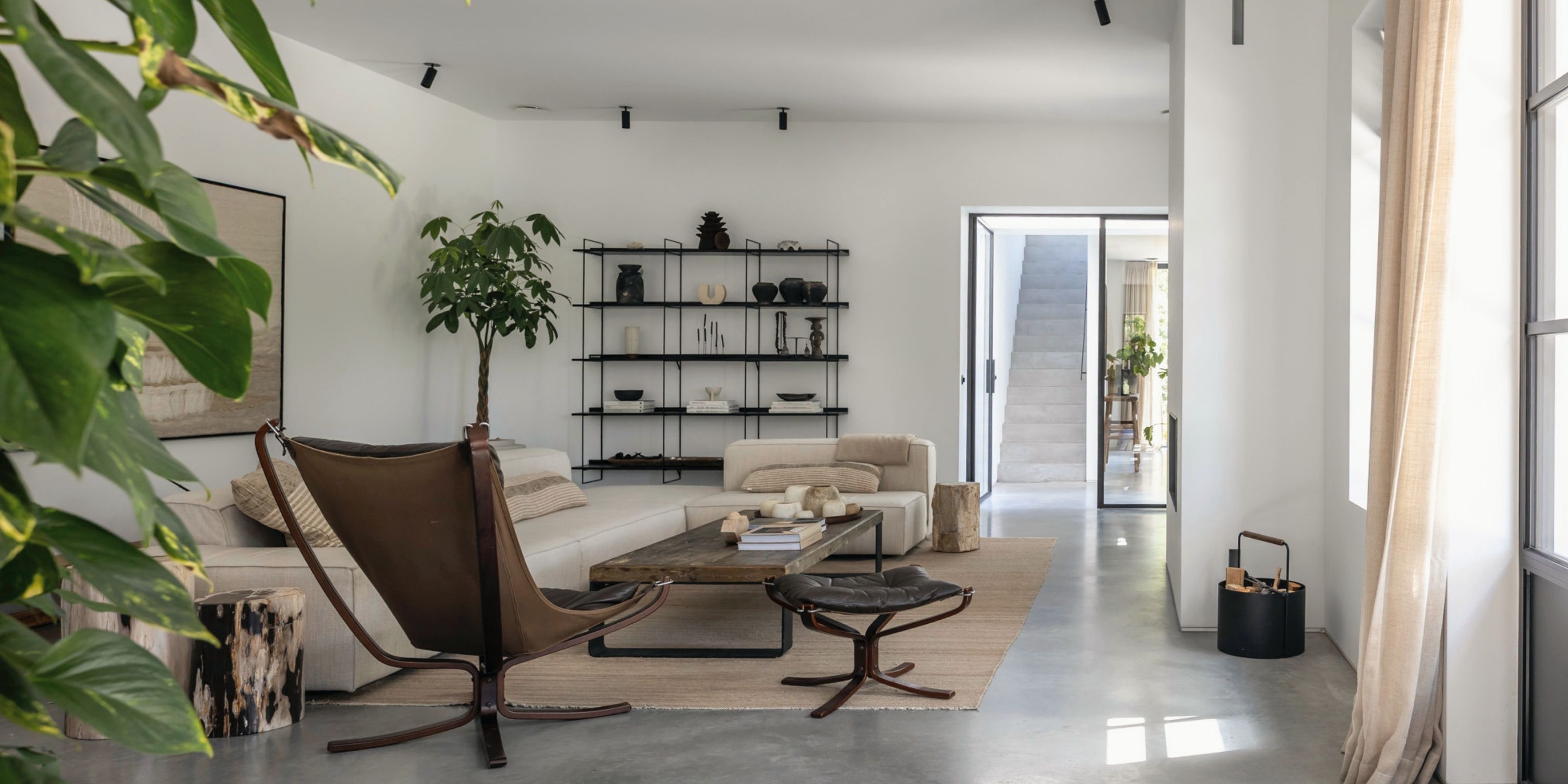 The living room as a shoot location: a leather sling chair, a low wooden table and a linen sofa on a jute rug, with a view through to the concrete staircase.