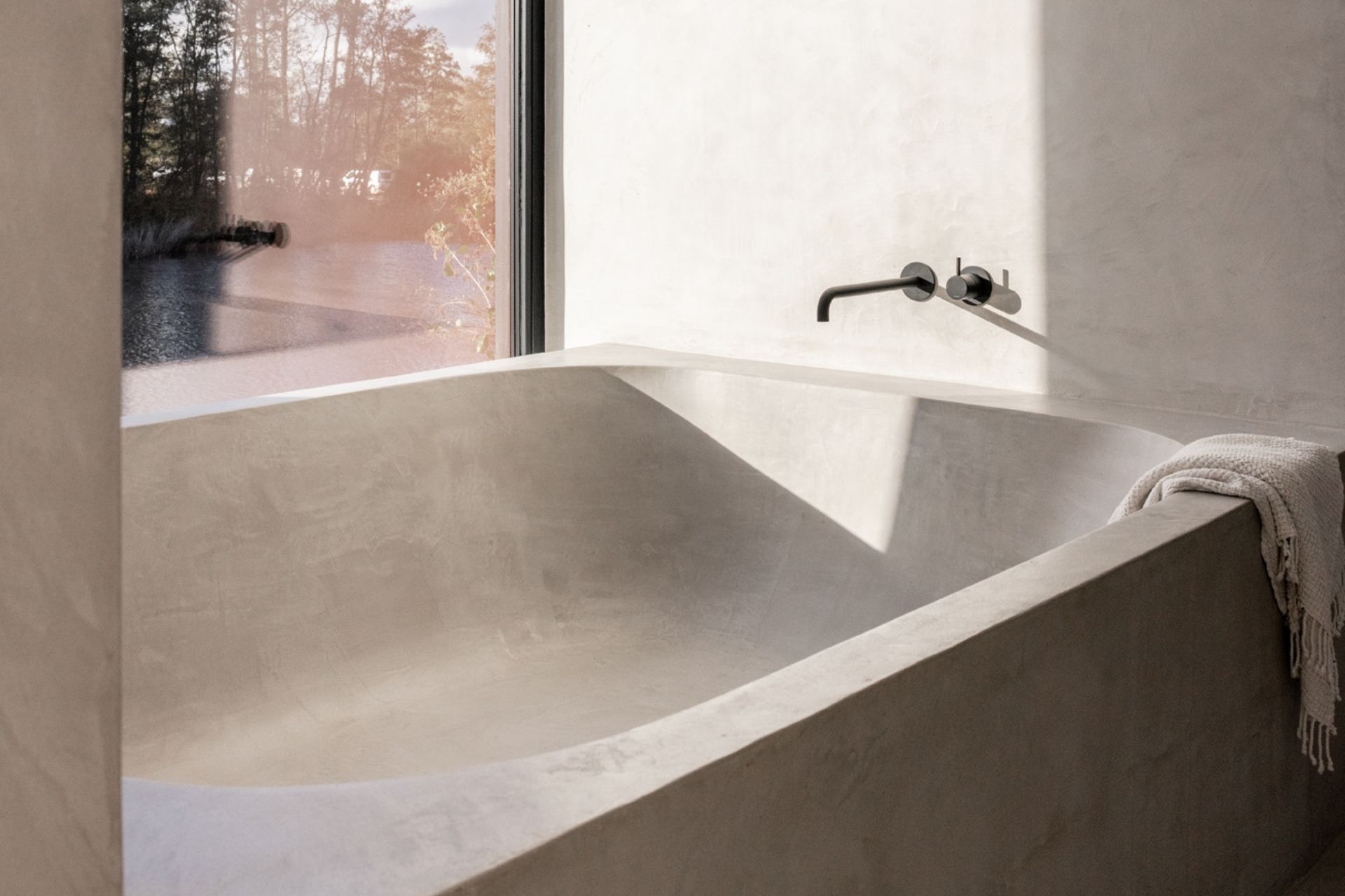 The microcement bath in the master bathroom, next to a full-height window looking out on the water and the trees.