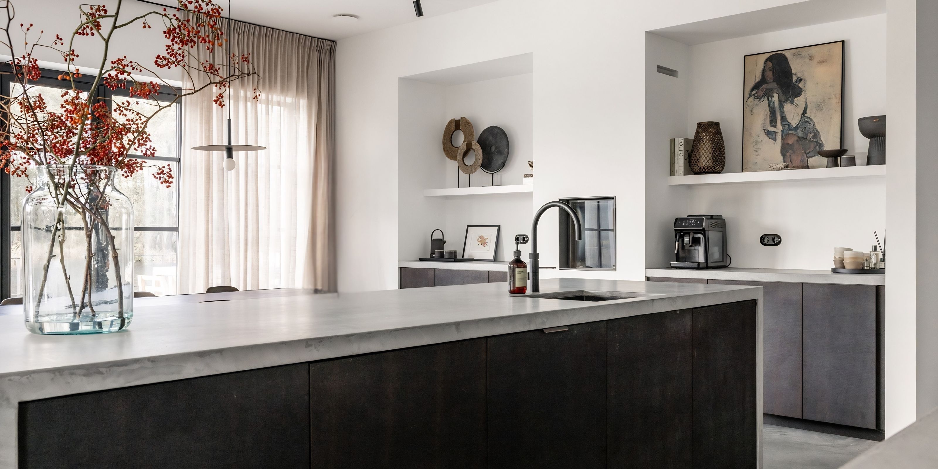 The kitchen island with a microcement worktop and smoked oak fronts, with branches of red berries in a glass vase.