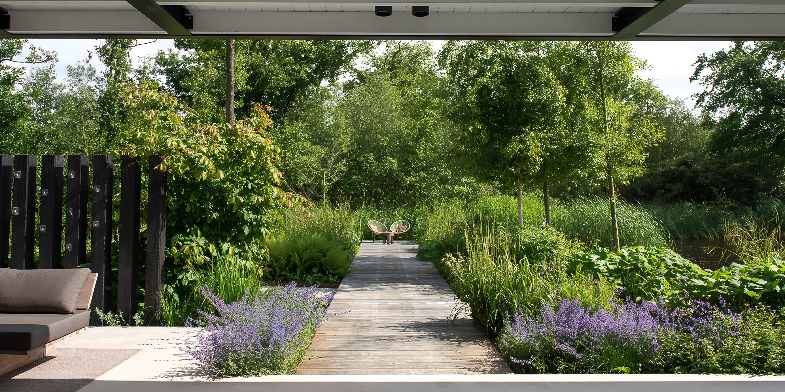 A wooden boardwalk leading through the landscape garden, between lavender and tall grasses, seen from under the canopy.